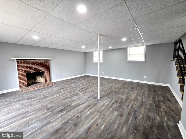 basement with dark hardwood / wood-style flooring, a brick fireplace, and a paneled ceiling