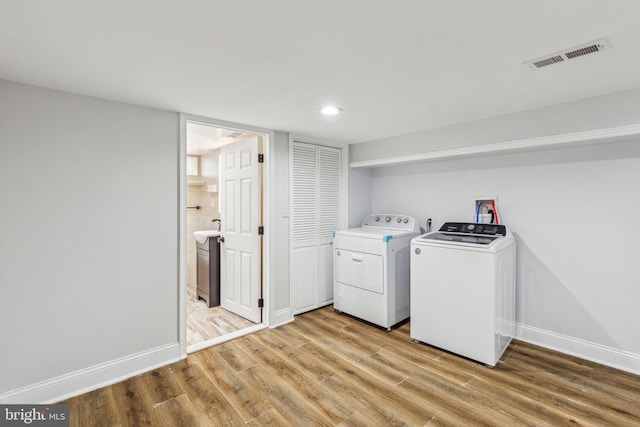 clothes washing area featuring visible vents, washer and clothes dryer, light wood-style floors, baseboards, and laundry area