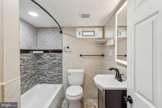 full bathroom with visible vents, toilet, tile walls, wainscoting, and vanity