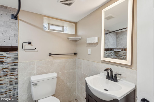 full bath with visible vents, toilet, tile walls, and vanity