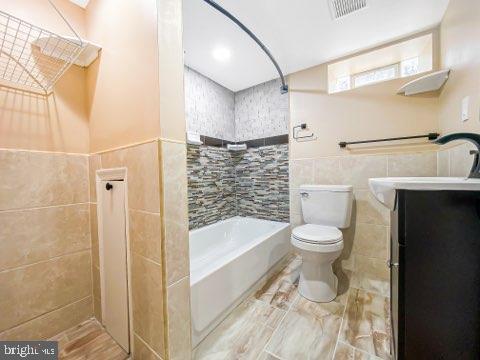 full bathroom featuring  shower combination, toilet, tile walls, and sink