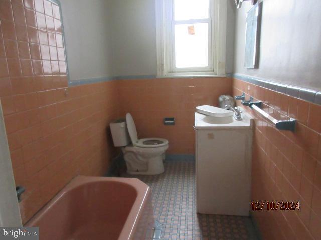 bathroom with vanity, a tub to relax in, toilet, and tile walls