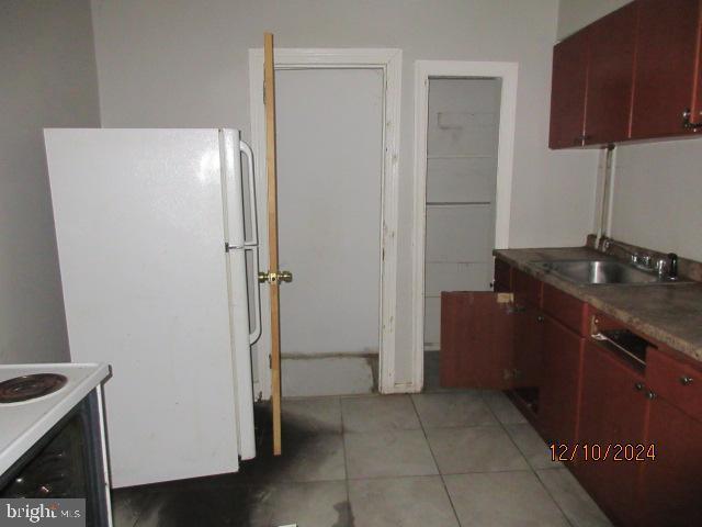 kitchen with white refrigerator, stove, light tile patterned floors, and sink