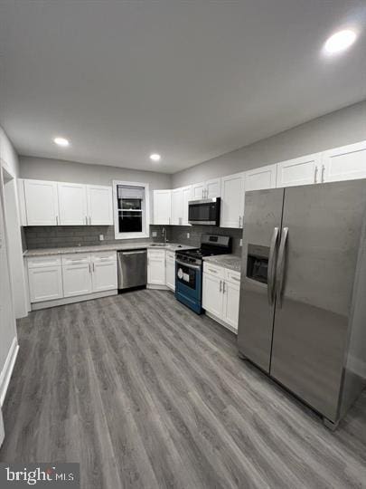 kitchen with backsplash, sink, hardwood / wood-style flooring, white cabinetry, and stainless steel appliances