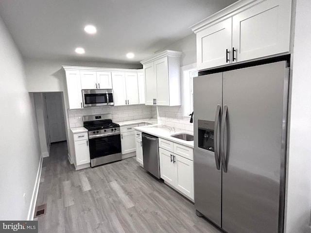 kitchen with tasteful backsplash, stainless steel appliances, sink, light hardwood / wood-style flooring, and white cabinetry