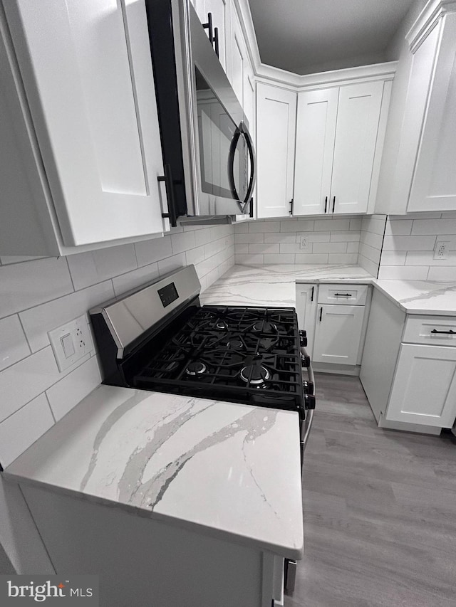 kitchen with black range with gas cooktop, white cabinetry, tasteful backsplash, and light stone counters