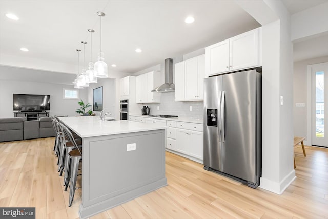 kitchen with a kitchen island with sink, wall chimney exhaust hood, appliances with stainless steel finishes, decorative light fixtures, and white cabinetry