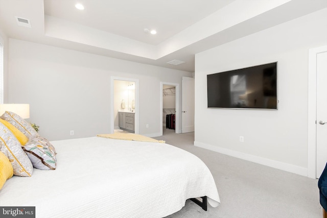 bedroom with a tray ceiling, connected bathroom, a walk in closet, and light colored carpet