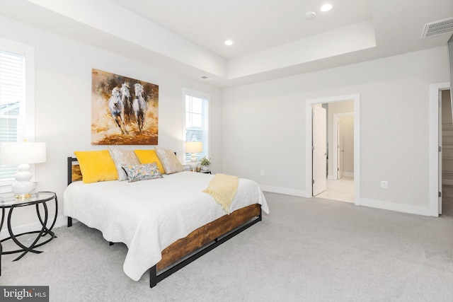 bedroom featuring a raised ceiling, connected bathroom, and light carpet