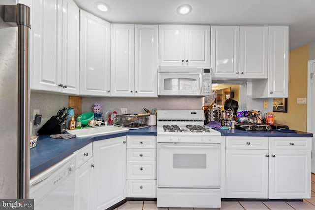 kitchen with light tile patterned floors, sink, white appliances, and white cabinets