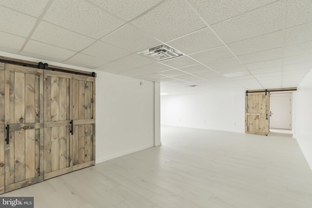 basement featuring hardwood / wood-style floors, a barn door, and a paneled ceiling