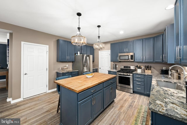 kitchen with appliances with stainless steel finishes, sink, blue cabinetry, light wood-type flooring, and a center island