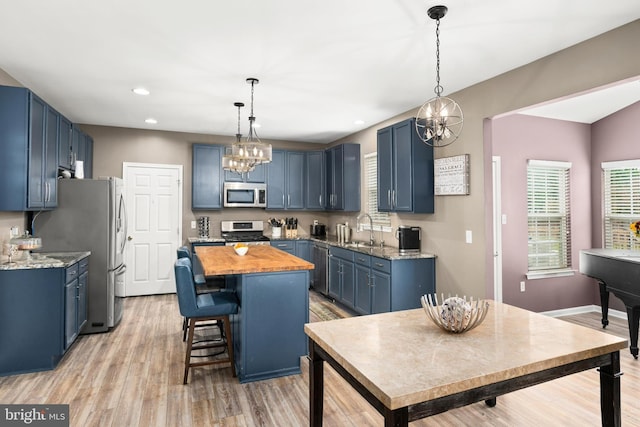 kitchen with light hardwood / wood-style flooring, appliances with stainless steel finishes, sink, blue cabinets, and an inviting chandelier