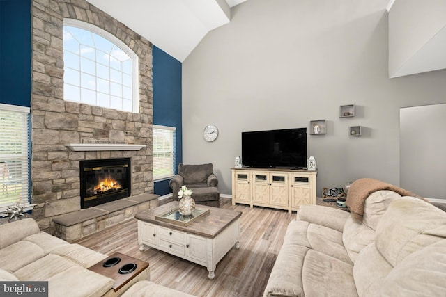 living room with light wood-type flooring, a stone fireplace, a wealth of natural light, and lofted ceiling