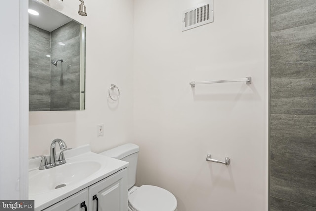 bathroom with a tile shower, vanity, and toilet