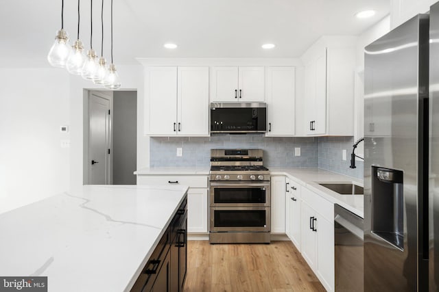 kitchen with white cabinets, sink, hanging light fixtures, appliances with stainless steel finishes, and light hardwood / wood-style floors