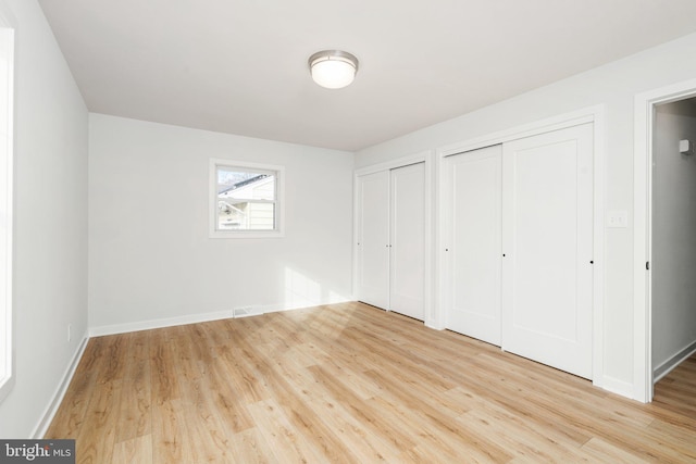 unfurnished bedroom with two closets and light hardwood / wood-style flooring