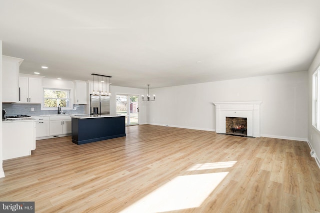 unfurnished living room featuring a healthy amount of sunlight, an inviting chandelier, sink, and light hardwood / wood-style flooring