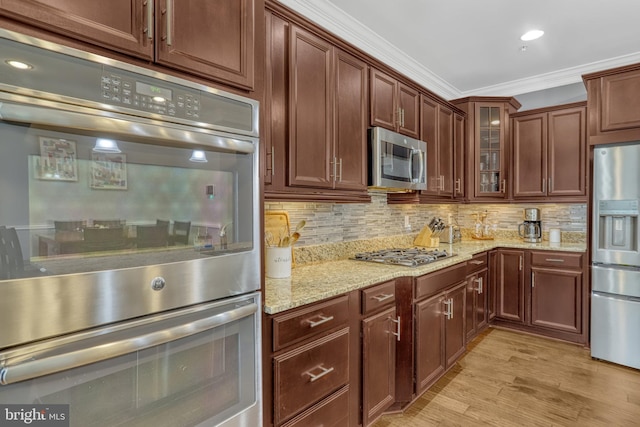 kitchen with backsplash, stainless steel appliances, light stone counters, and crown molding