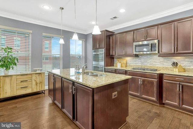 kitchen featuring a center island with sink, crown molding, decorative light fixtures, light stone counters, and stainless steel appliances