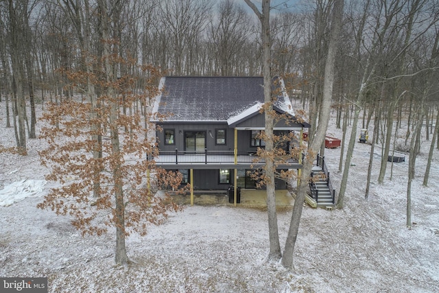 snow covered rear of property featuring roof with shingles, stairs, and a deck