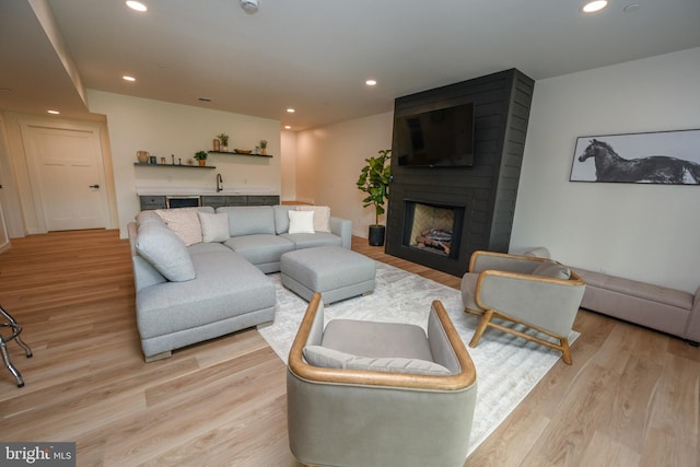 living area featuring bar with sink, light wood-type flooring, recessed lighting, and a large fireplace