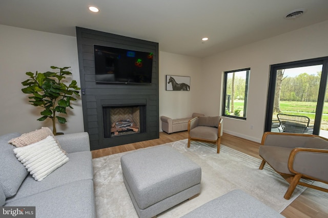 living area featuring wood finished floors, a large fireplace, recessed lighting, and baseboards