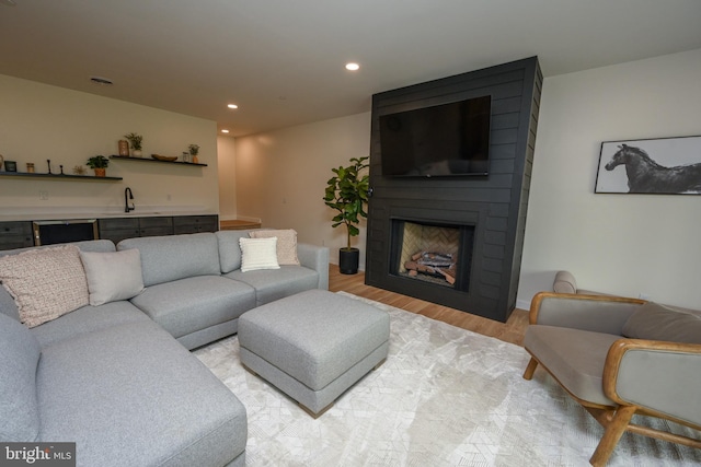 living room featuring light wood-style flooring, bar with sink, recessed lighting, and a fireplace