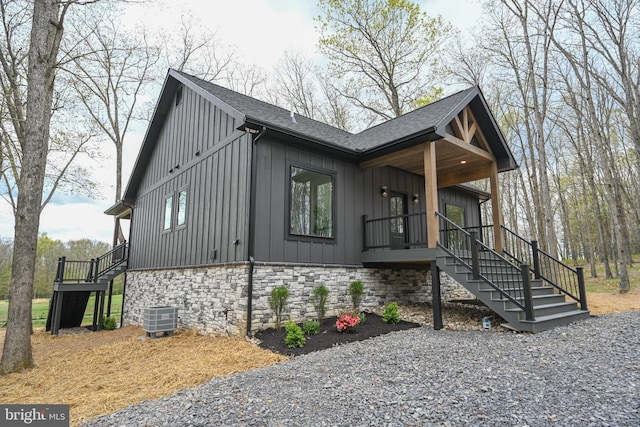 view of property exterior with stairway, board and batten siding, cooling unit, stone siding, and a shingled roof