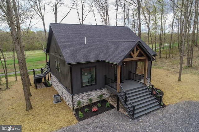 chalet / cabin featuring a shingled roof, stone siding, board and batten siding, cooling unit, and covered porch