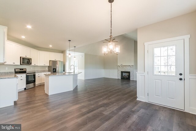 kitchen featuring appliances with stainless steel finishes, dark wood-type flooring, decorative light fixtures, white cabinets, and an island with sink