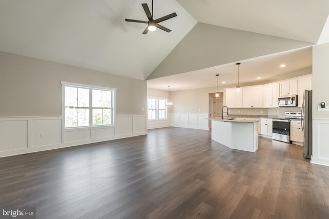 kitchen featuring high vaulted ceiling, white cabinets, hanging light fixtures, an island with sink, and stainless steel appliances