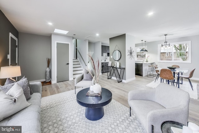 living room with a skylight, sink, light hardwood / wood-style floors, and an inviting chandelier