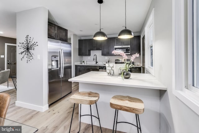 kitchen featuring a breakfast bar, light hardwood / wood-style flooring, appliances with stainless steel finishes, decorative light fixtures, and kitchen peninsula