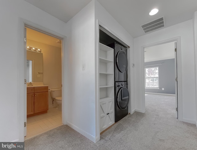 corridor featuring light colored carpet, sink, and stacked washer and clothes dryer