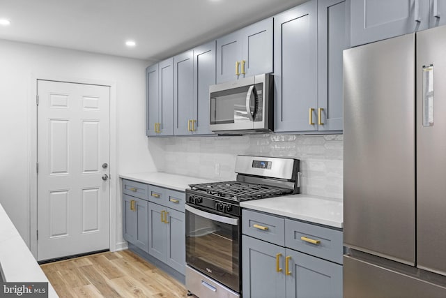 kitchen with backsplash, gray cabinets, light wood-type flooring, and appliances with stainless steel finishes