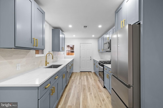 kitchen featuring decorative backsplash, light stone countertops, light wood-type flooring, stainless steel appliances, and sink