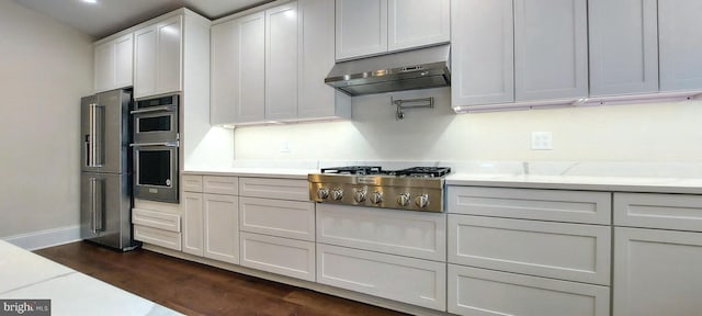 kitchen with light stone countertops, range hood, dark hardwood / wood-style flooring, white cabinetry, and stainless steel appliances