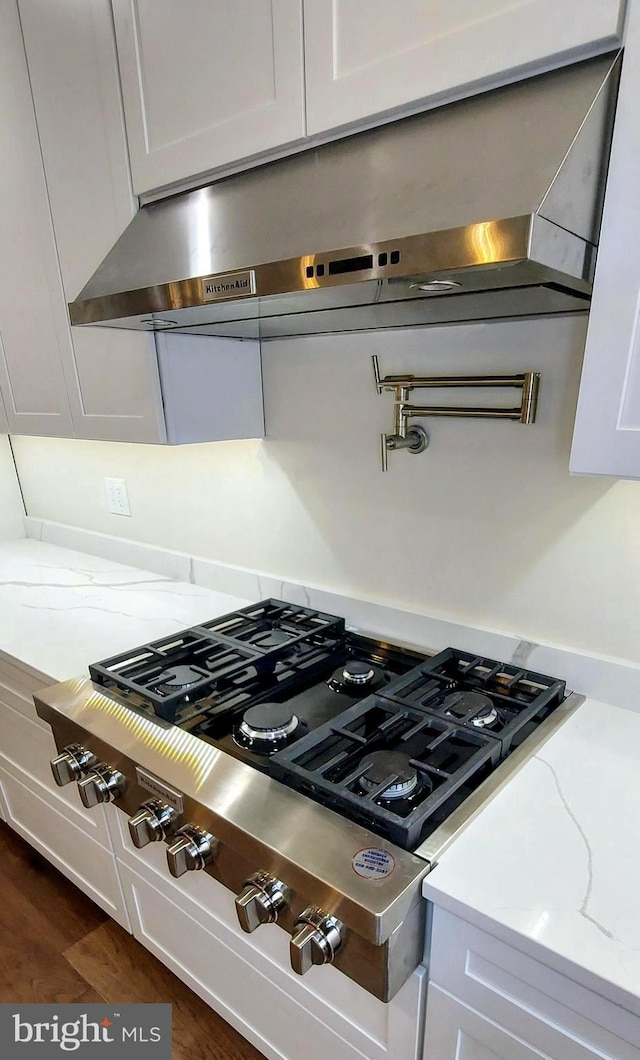 details with dark hardwood / wood-style flooring, light stone counters, stainless steel gas cooktop, exhaust hood, and white cabinetry