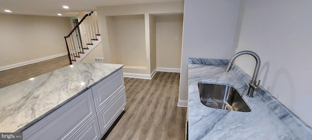 kitchen featuring white cabinets, light hardwood / wood-style floors, light stone counters, and sink