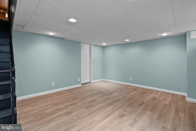 basement featuring a paneled ceiling and light hardwood / wood-style flooring