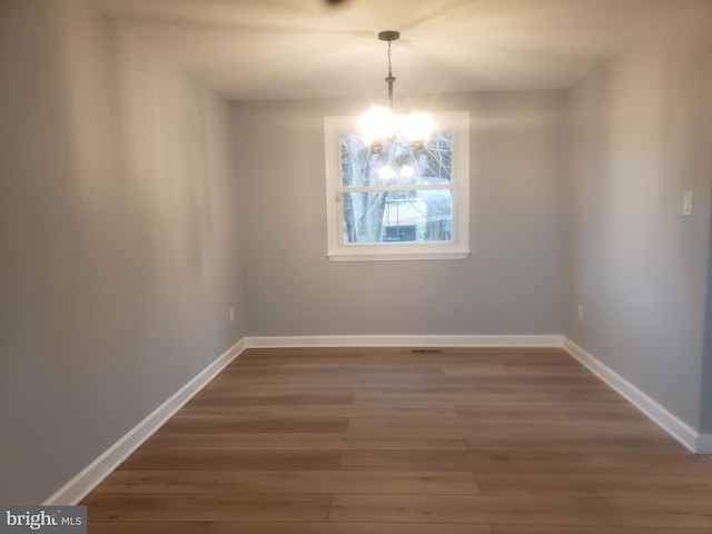 unfurnished dining area featuring a chandelier and wood-type flooring