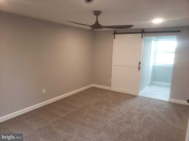 spare room featuring carpet, a barn door, and ceiling fan