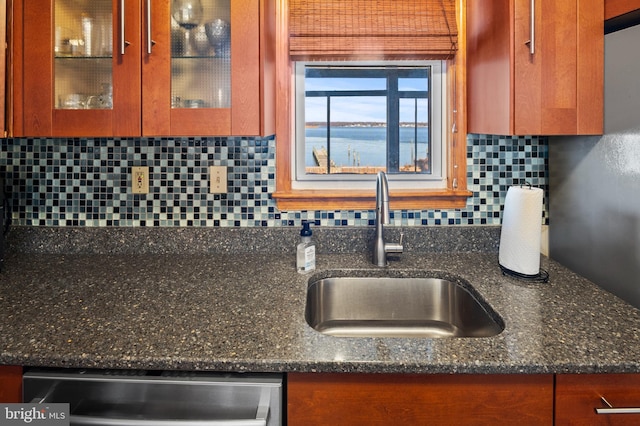 kitchen with dishwasher, sink, dark stone countertops, decorative backsplash, and a water view