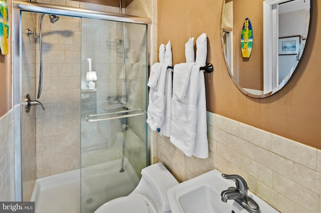 bathroom with toilet, tile walls, a shower with shower door, and sink