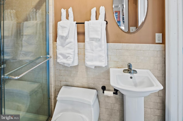 bathroom with toilet, a shower with shower door, and tile walls