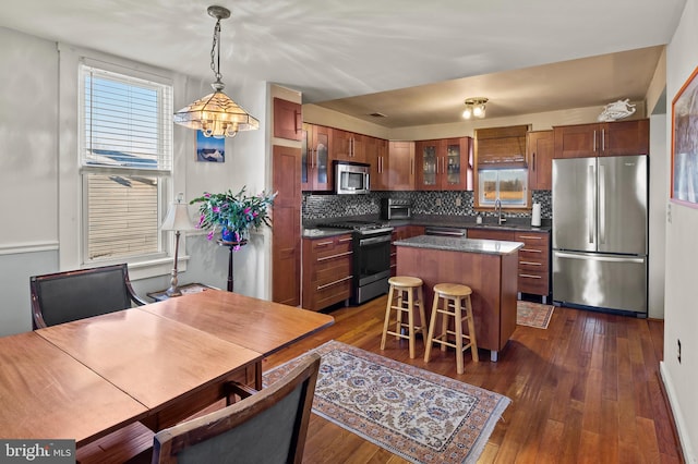 kitchen with backsplash, stainless steel appliances, dark wood-type flooring, a center island, and hanging light fixtures