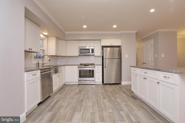 kitchen with tasteful backsplash, light hardwood / wood-style floors, white cabinetry, stainless steel appliances, and light stone counters