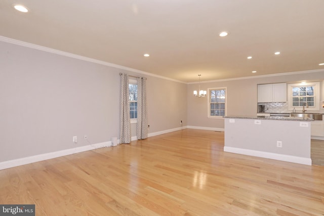 unfurnished living room with light wood-type flooring, an inviting chandelier, crown molding, and sink