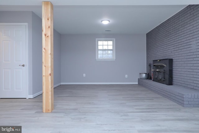 unfurnished living room with brick wall, light hardwood / wood-style floors, and a wood stove